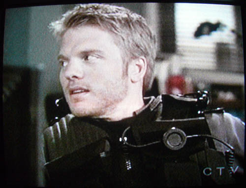 Photo of TV screen: David Paetkau, in combat vest, turns his head to the side