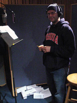 Jeremy Harris, in hoodie, toque, and headphones, stands amid crumpled pages in a recording booth