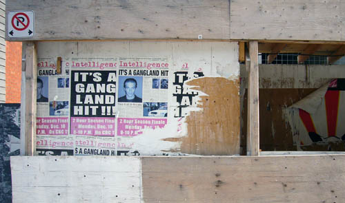 Decaying posters on construction hoarding read Intelligence IT'S A GANGLAND HIT!