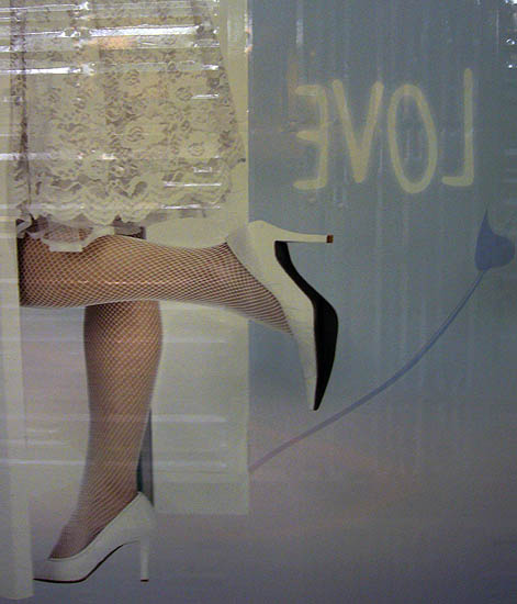 Corner of a wall poster shows the word LOVE backwards and a woman in a lacy white skirt and white fishnets kicking up one heel