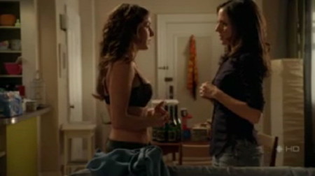 Erica, in black bra, watches Cassidy unbutton her own shirt