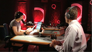 Ghomeshi interviews guest in radio studio with glowing red ‘Q’ backdrops