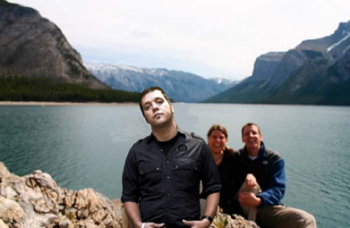 Strombo staring out at us in front of woman and man at mountainside lake