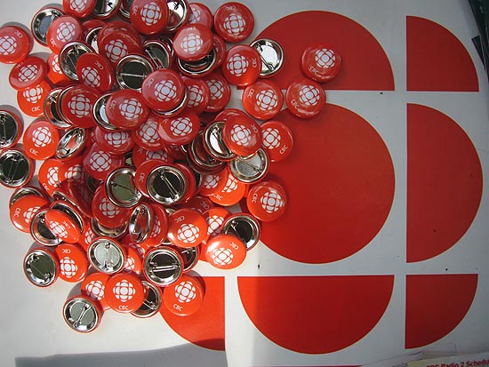 Mass of red CBC lapel buttons atop red CBC logo