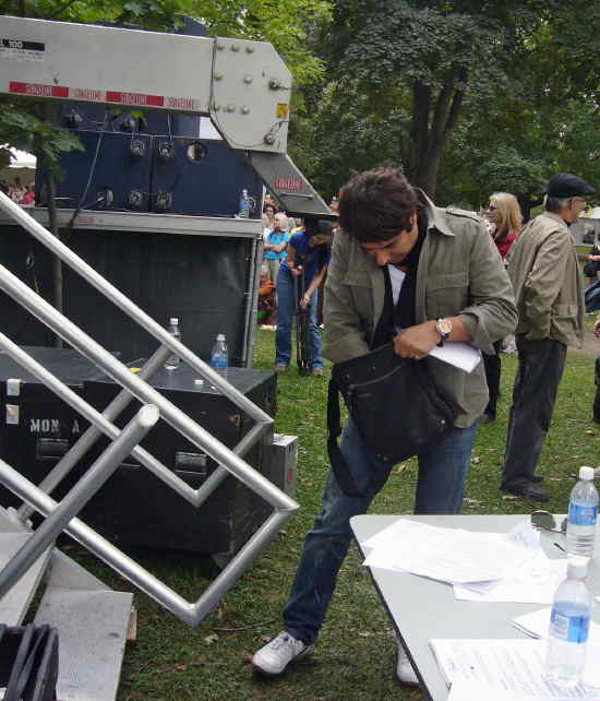 Jian Ghomeshi roots in his manpurse near an aluminum staircase