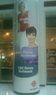 Poster on column of building advertising CBC News Network and two news anchors